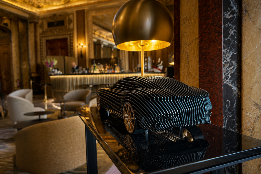Steve Chaudanson Aston Martin DB11 Gillis Green contemporary sculpture with gold wheels displayed in a luxury hotel lounge.