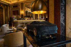 Steve Chaudanson Aston Martin DB11 Gillis Green contemporary sculpture with gold wheels displayed in a luxury hotel lounge.